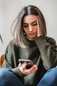 Vrouw ervaart digitaal conflict en kijkt bezorgd naar smartphone – illustratie voor online problemen en rechtsbijstandverzekering.