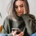 Vrouw ervaart digitaal conflict en kijkt bezorgd naar smartphone – illustratie voor online problemen en rechtsbijstandverzekering.